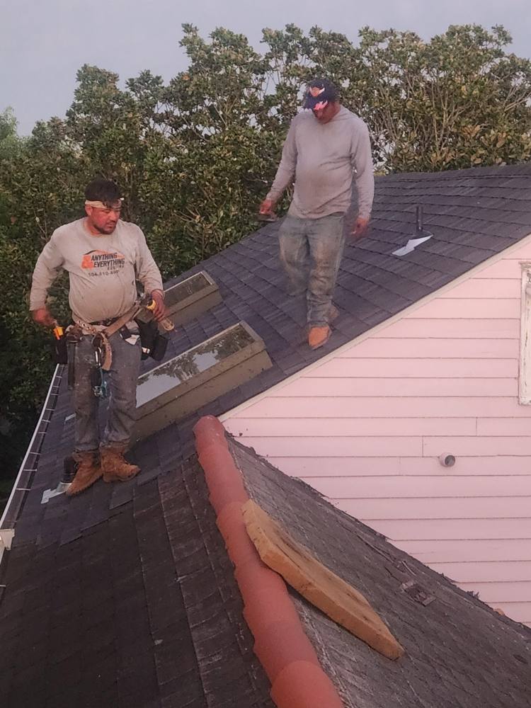 Two roofers on a roof next to a pink wall