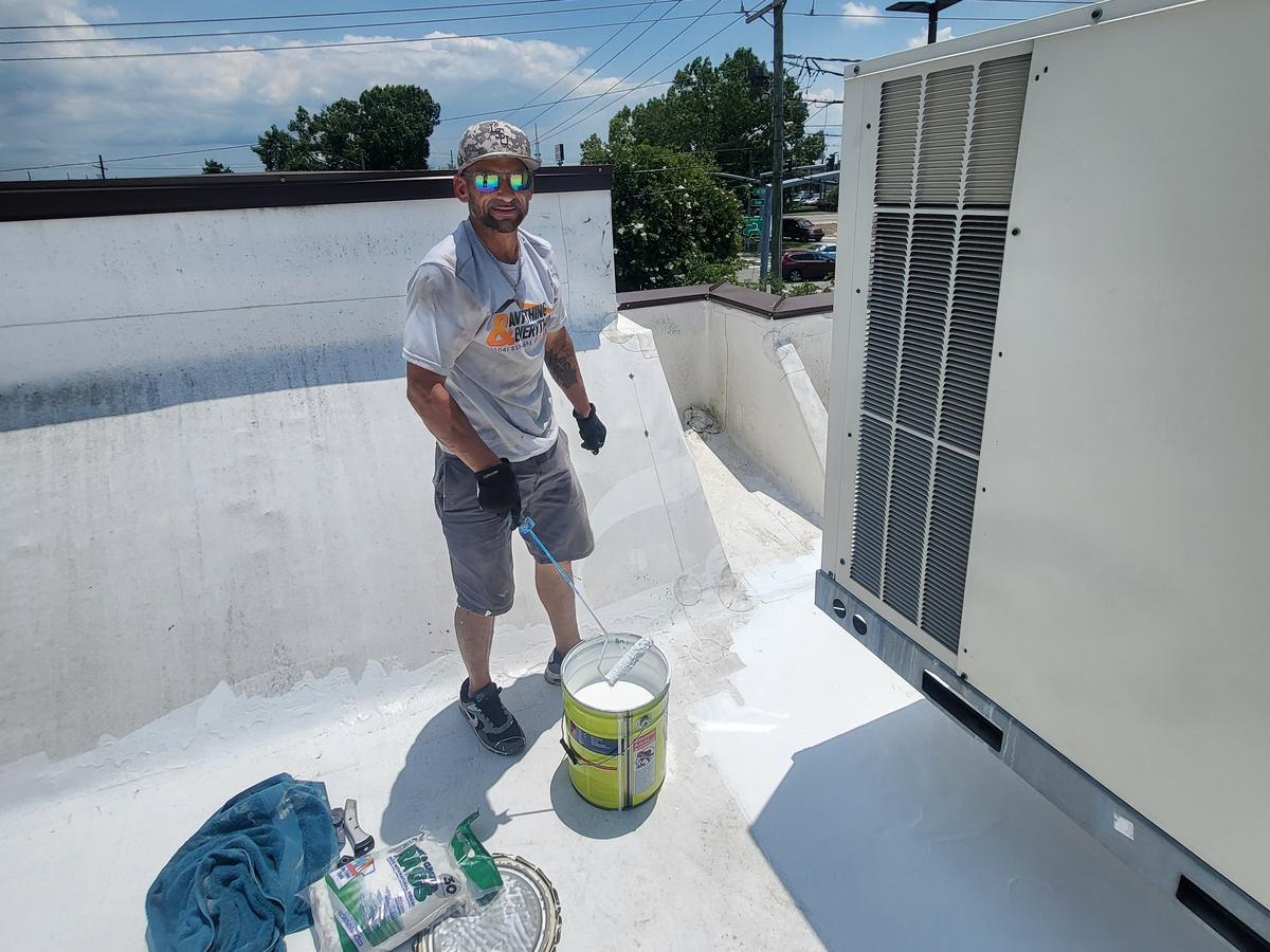 Roofer applying white coating on a commercial flat roof next to an AC unit
