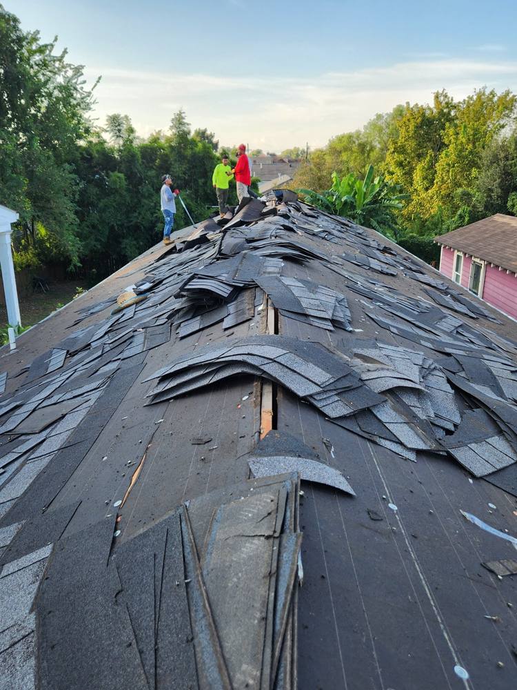 Roof tear-off in progress with crew at the ridge